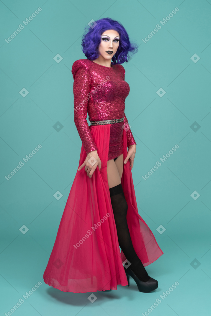 Drag queen en robe rose tenant une jupe en marchant