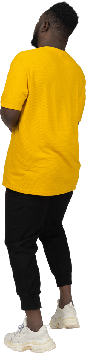 Three-quarter back view of a young dark-skinned man in yellow t-shirt