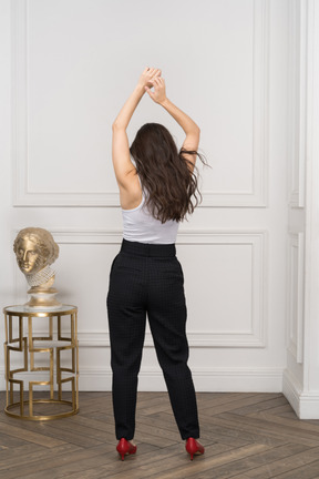 Back view of a young female raising hands while standing by a golden greek sculpture