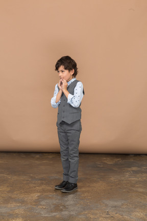 Vue de face d'un garçon en costume gris faisant un geste de prière