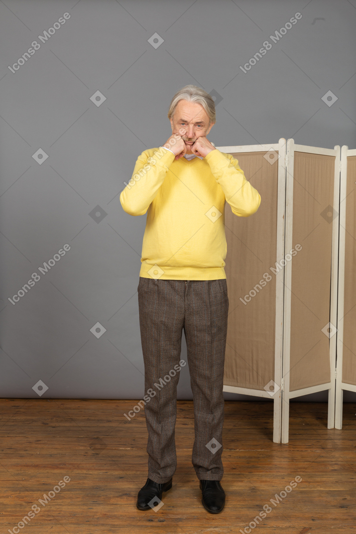 Vista frontal de un anciano apretando los puños y tocando la cara
