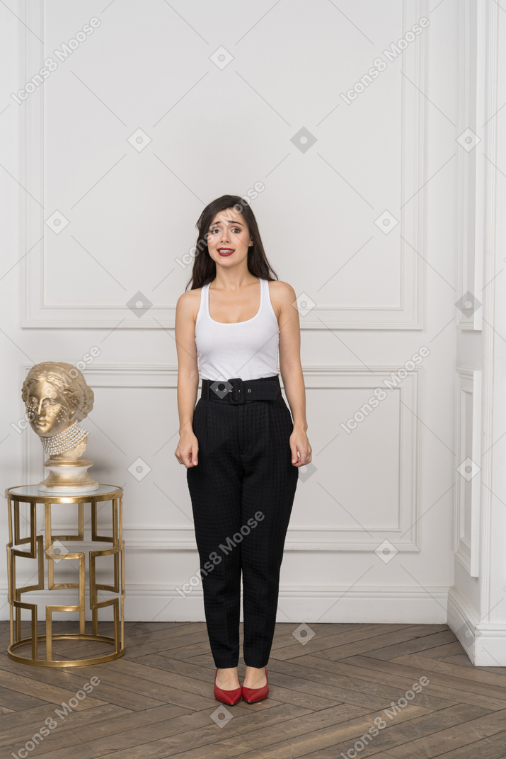 Front view of a confused young female standing by golden greek sculpture