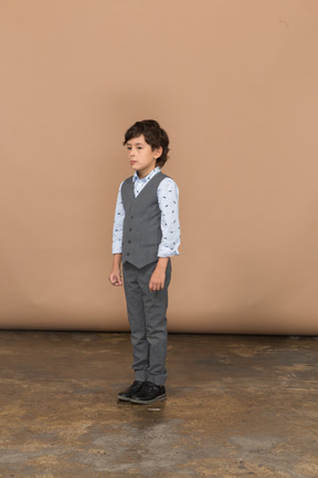 Front view of a seirous boy in grey suit standing still