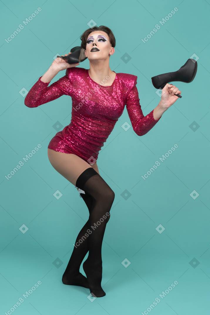 Drag queen in pink dress holding a pair of black pumps