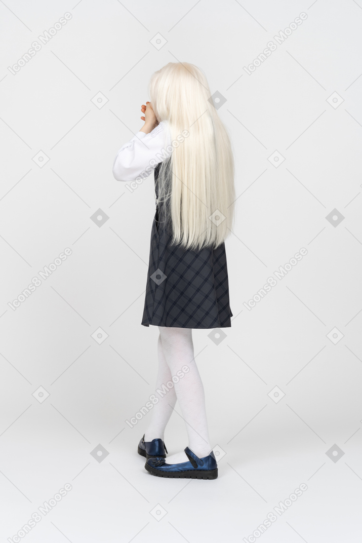 Back view of a schoolgirl covering mouth with hands