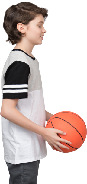 Vista lateral de un niño sosteniendo una pelota de baloncesto