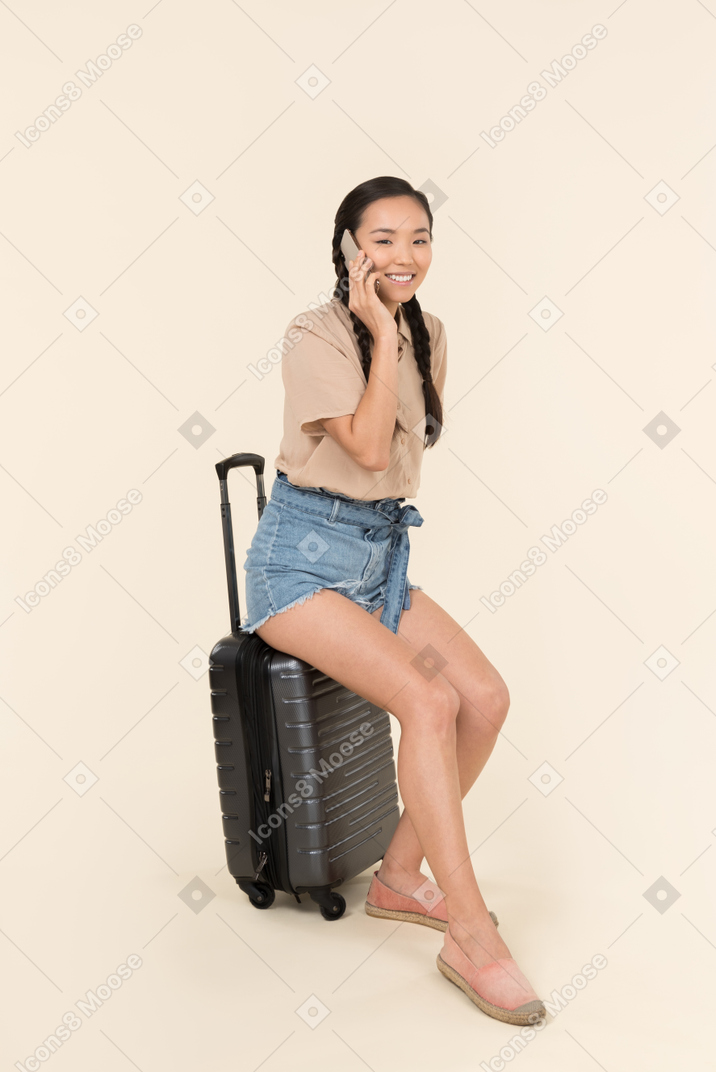 젊은 여성 여행자 가방에 앉아서 전화 통화