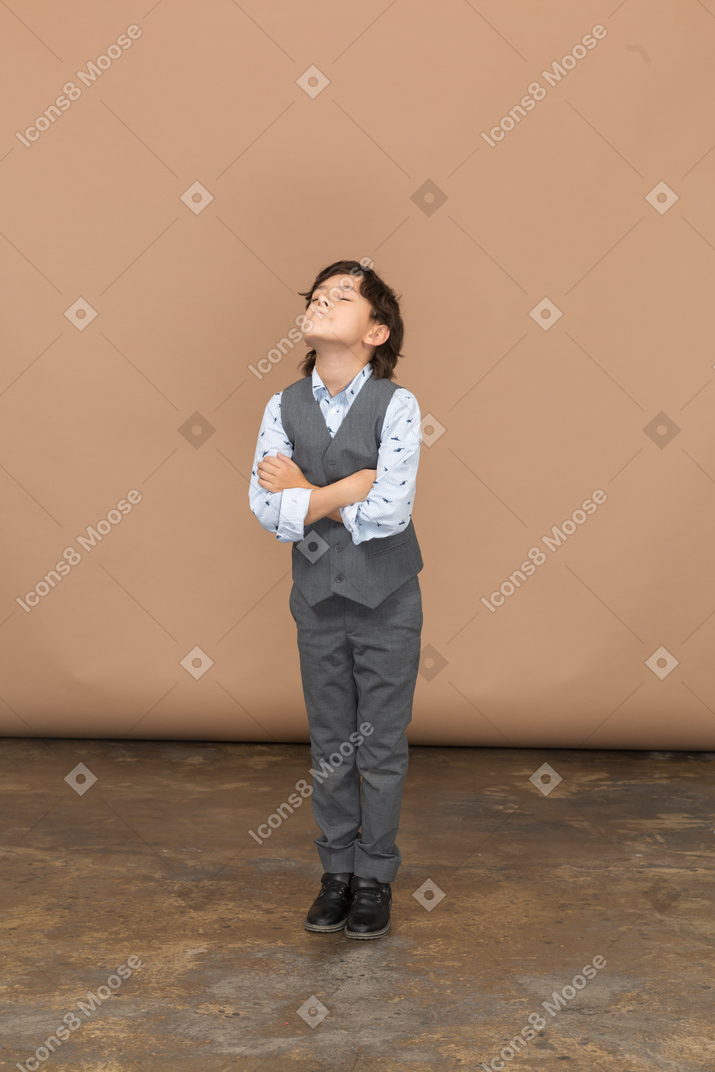 Vista frontal de un niño con traje gris de pie con los brazos cruzados