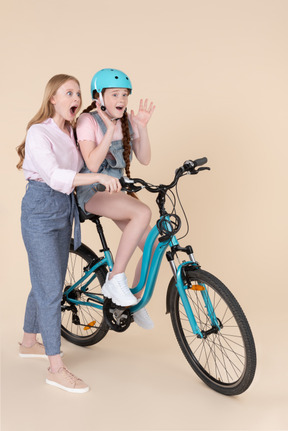 Surprised young woman teaching scared teenage girl how to ride the bicycle