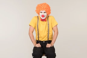 Male clown in red wig sitting on the chair
