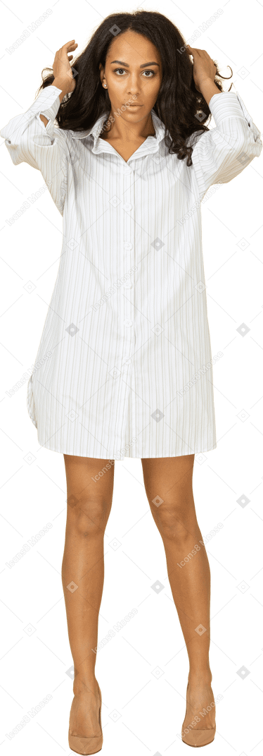Vista frontal de una mujer joven de piel oscura con vestido blanco arreglando su cabello