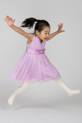 팔과 다리를 벌리고 점프하는 핑크색 드레스를 입은 소녀