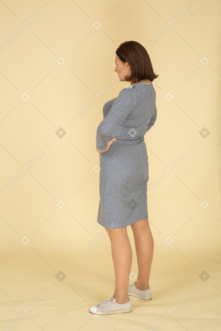 腰に手でポーズをとって灰色のドレスを着た女性の側面図
