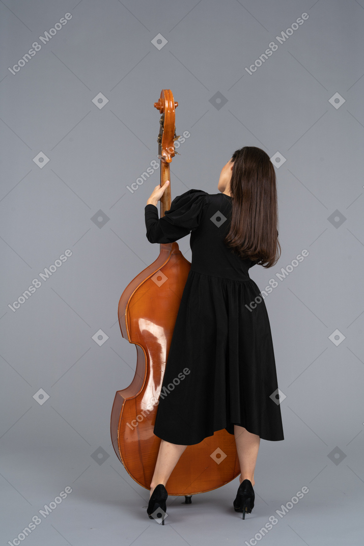 Back view of a young female musician in black dress holding her double-bass