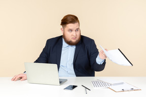Giovane uomo in sovrappeso seduto al tavolo e in possesso di documenti