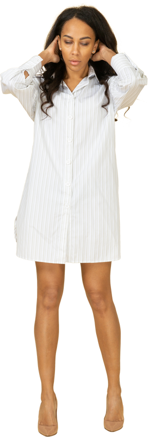 Вид спереди темнокожей молодой девушки в белом платье, поправляющей прическу