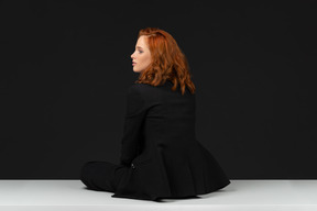 A back side view of the beautiful young woman dressed in black and sitting on the white table