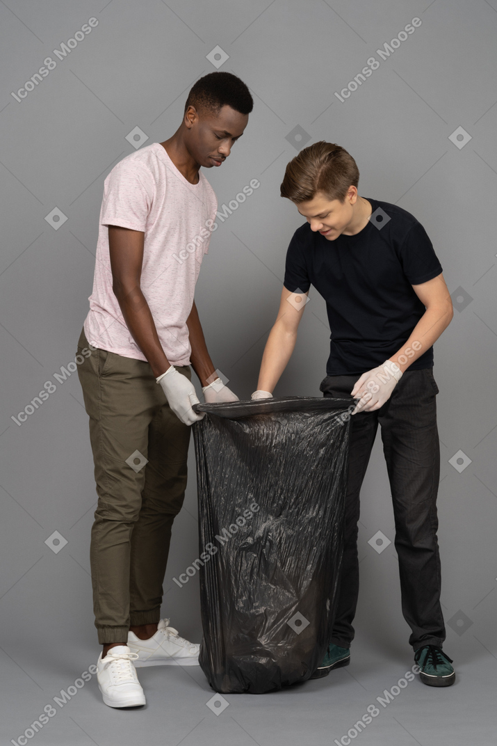 Two young men looking inside a trash bag