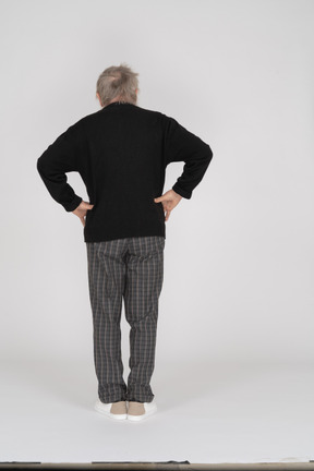 Uomo anziano con le mani sui fianchi in piedi con la schiena verso la telecamera