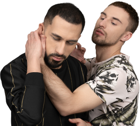Young caucasian man holding another man sensually by the neck in a half-hug