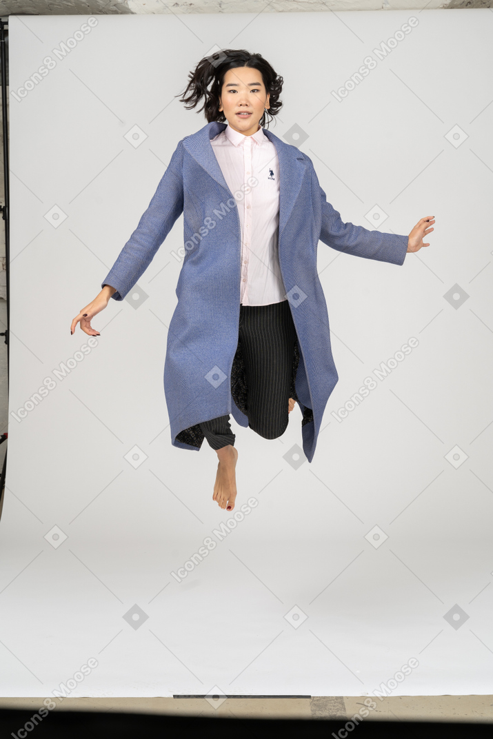 Woman in coat jumping and looking at camera
