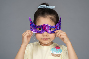 Primo piano di una bambina che prova una maschera da supereroe