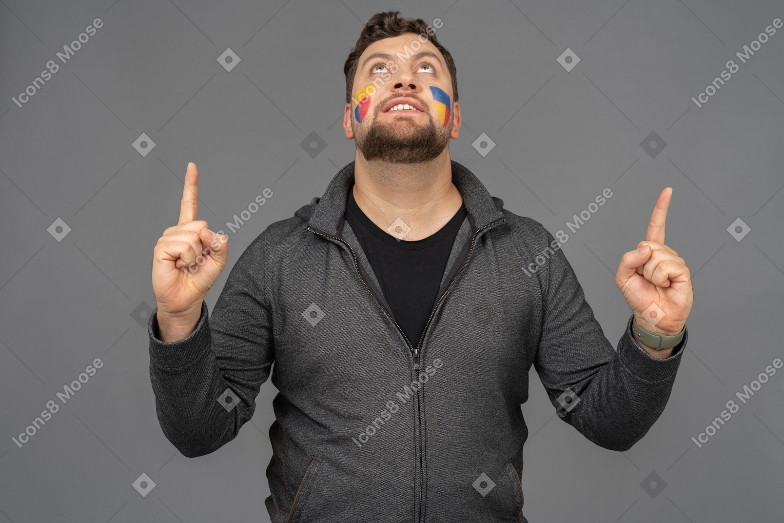 Vista frontal de um fã de futebol masculino com arte colorida no rosto levantando os dedos