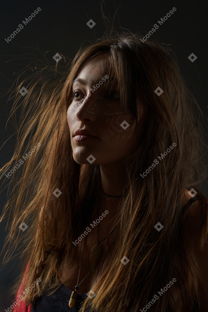 Retrato de três quartos de uma jovem mulher com arte facial étnica e cabelo bagunçado