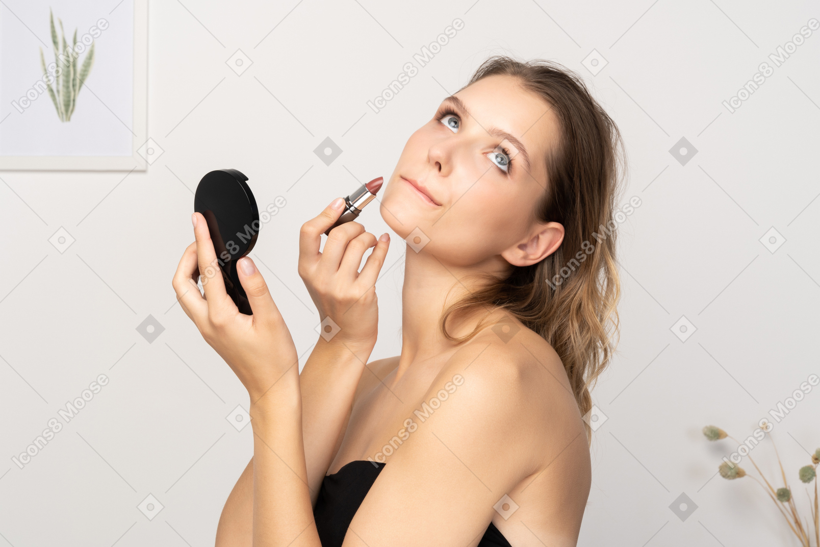 Side view of a young woman applying lipstick while holding a mirror