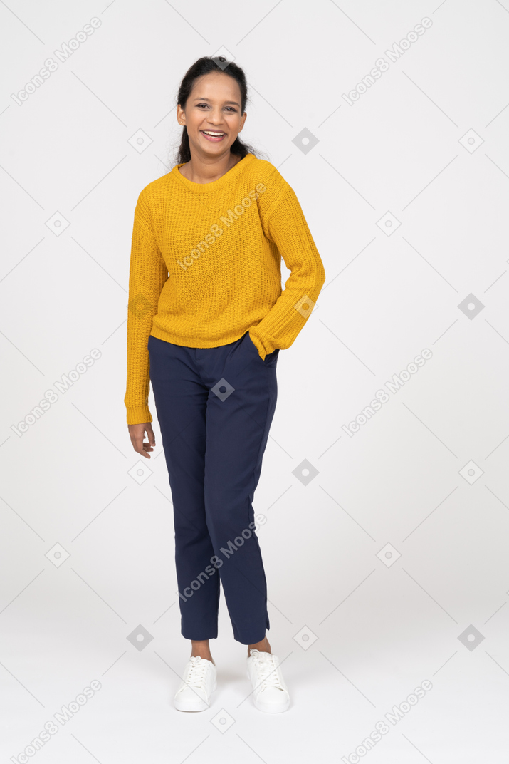 Vista frontal de una niña feliz en ropa casual posando con la mano en el bolsillo