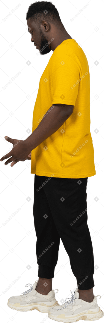 노란 티셔츠를 입은 사려깊은 몸짓을 하는 짙은 피부의 젊은 남자의 측면