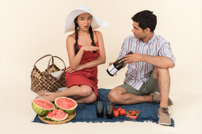 Young guy showing bottle of wine on a picnic to a woman which seems outraged