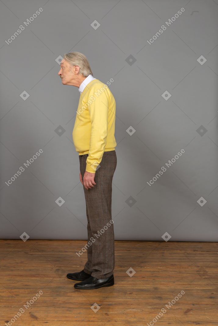 Vista laterale di un vecchio uomo sorpreso in pullover giallo sporgendosi in avanti e guardando da parte