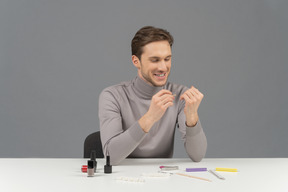 A cheerful young man doing his nails