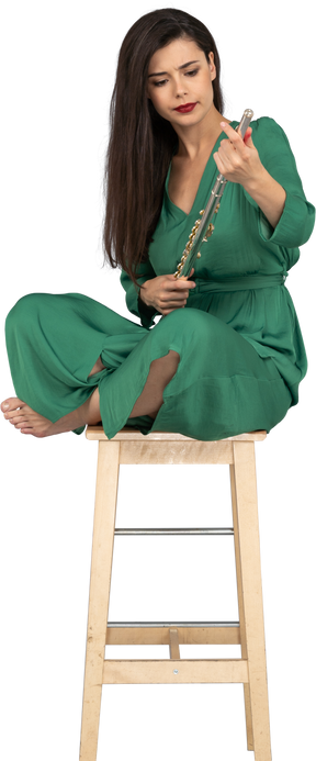 A figura intera di una giovane donna che tiene il clarinetto seduta con le gambe incrociate su una sedia di legno