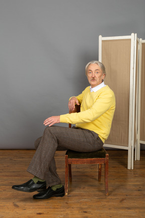 Mann mittleren alters, der auf einem stuhl sitzt und in die kamera schaut