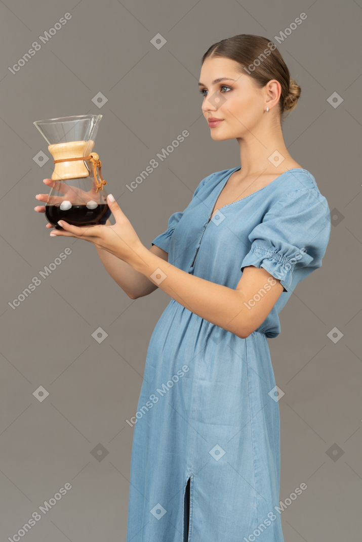 Three-quarter view of a young woman in blue dress holding a pitcher of wine