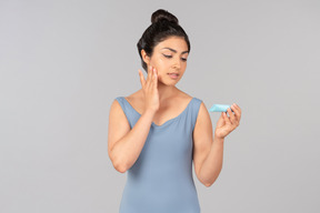 Jeune femme indienne en débardeur bleu appliquant la crème pour le visage