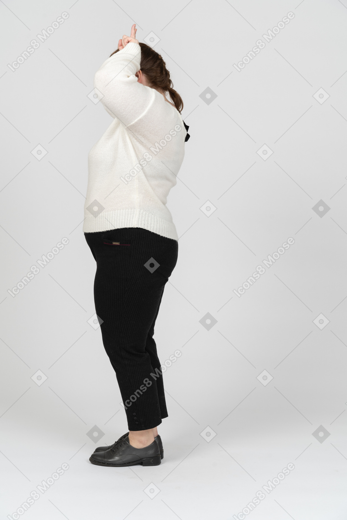 Vista laterale di una donna grassoccia in abiti casual che fa le corna