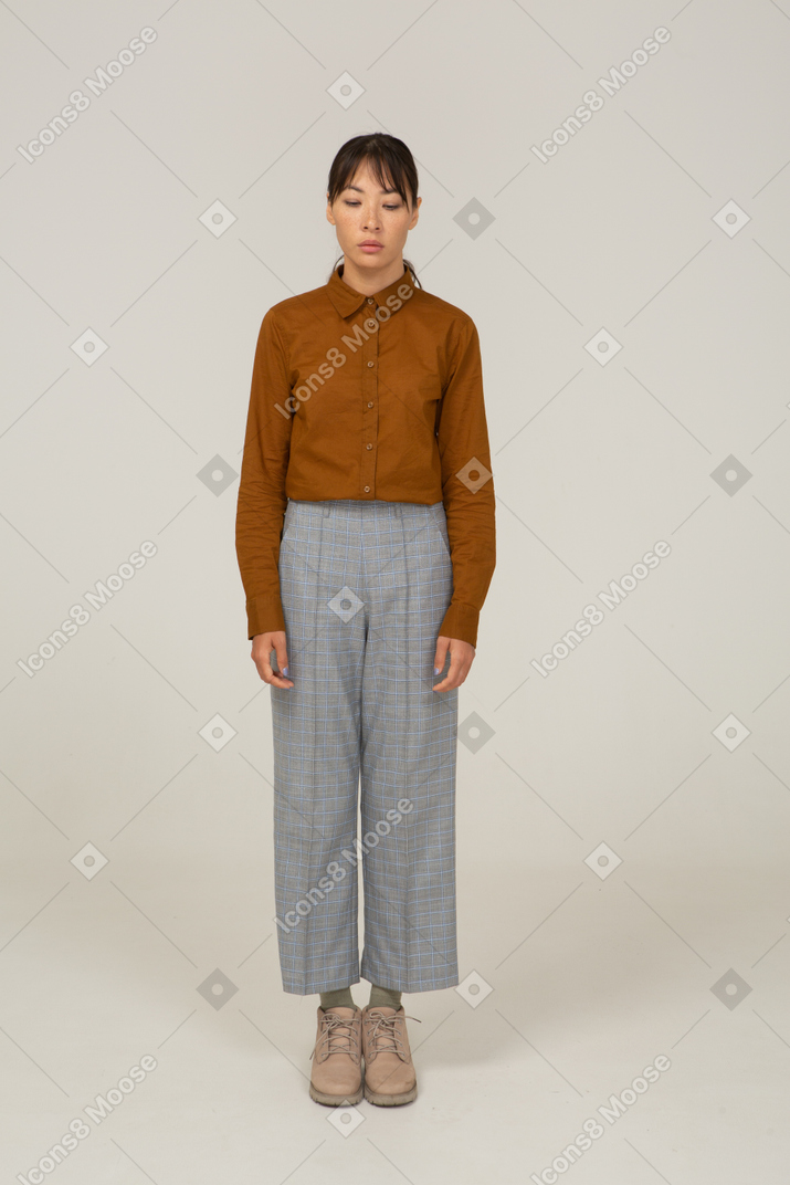 Vista frontal de uma jovem mulher asiática de calça e blusa, parada