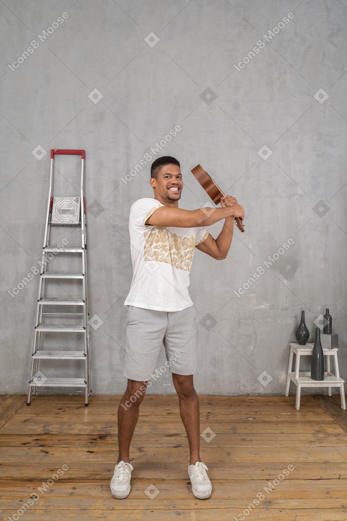 Front view of a man swinging an ukulele angrily like a bat