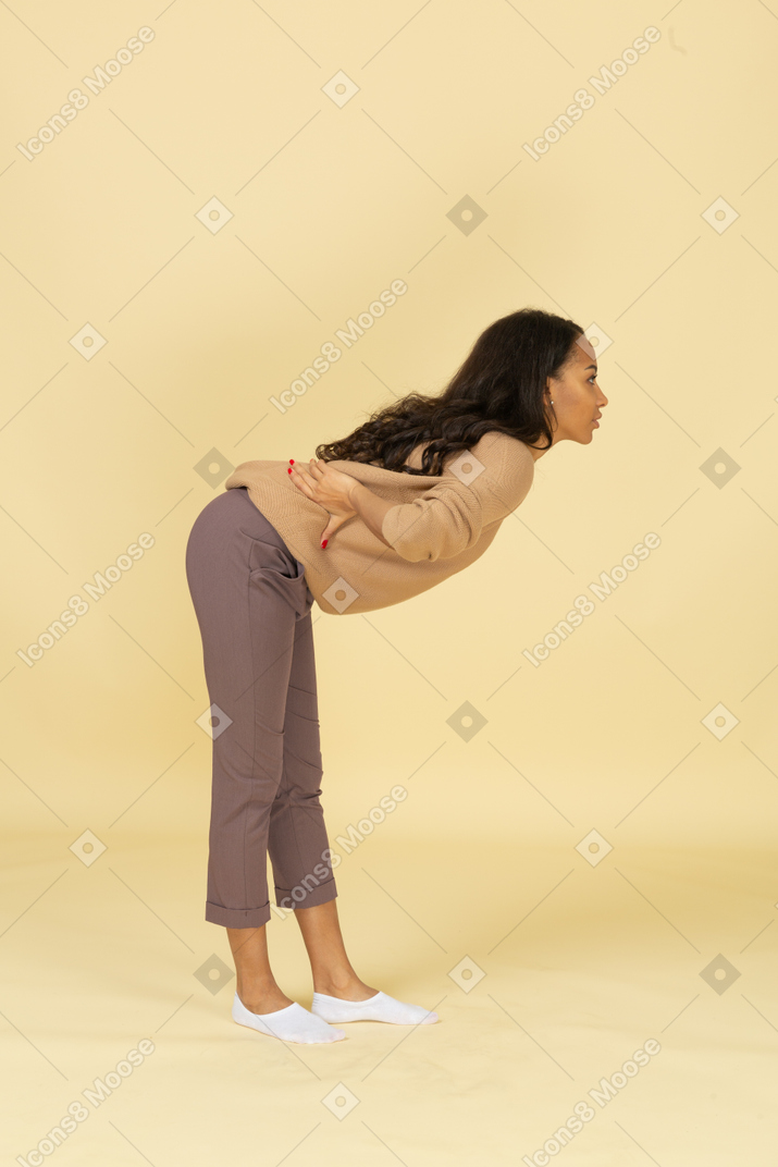腰に手を置いている間、前かがみに傾いている浅黒い肌の若い女性の側面図