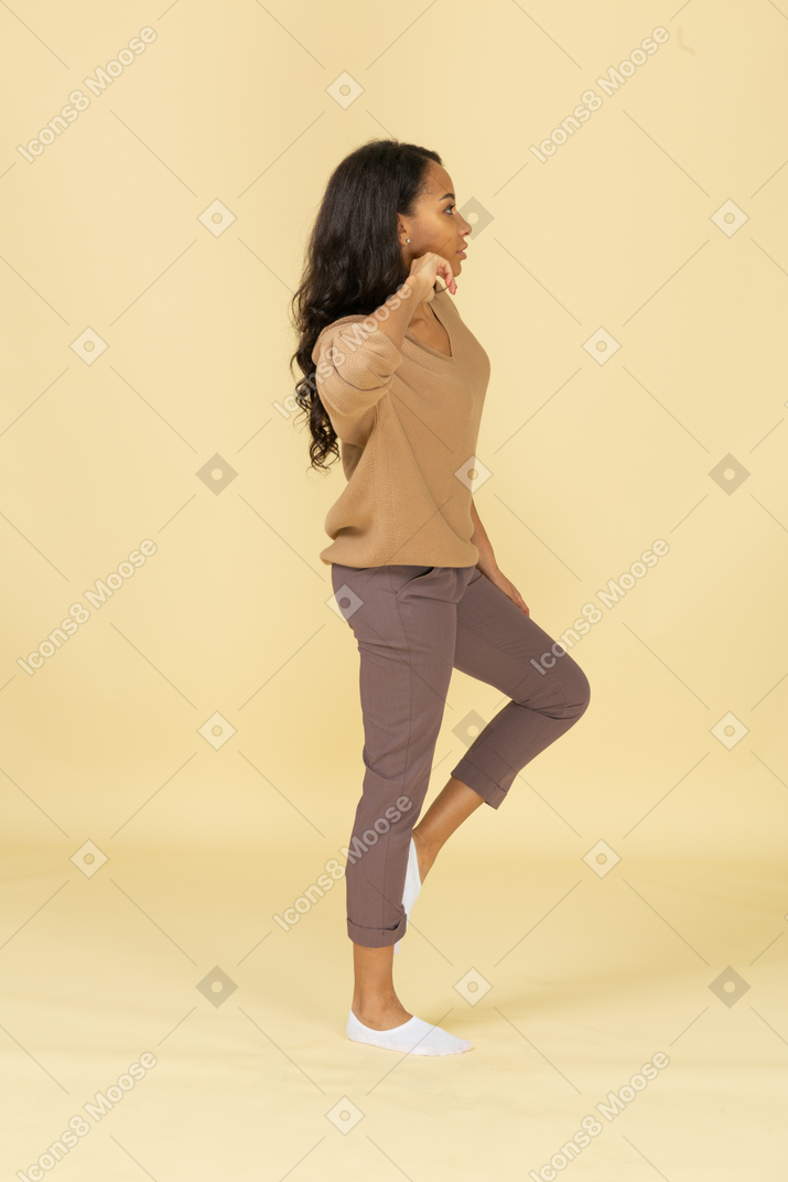 Vista lateral de uma jovem mulher de pele escura tocando o pescoço enquanto levanta a perna