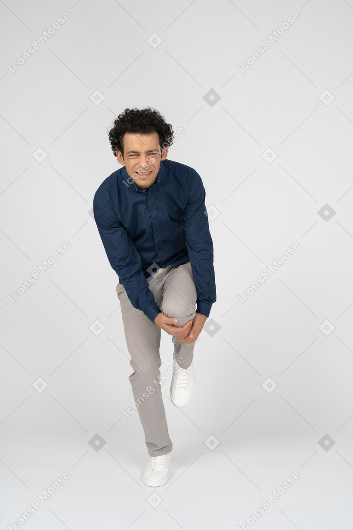 Vista frontal de un hombre en ropa casual tocando su rodilla lastimada