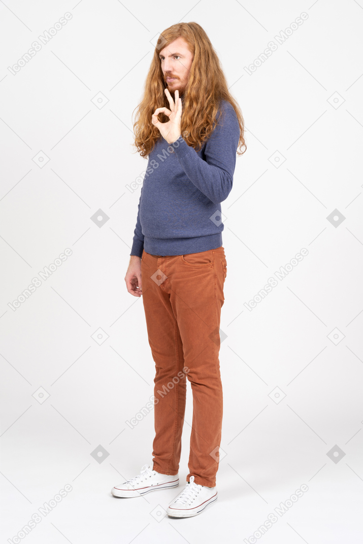 Vista lateral de un joven con ropa informal que muestra el signo de ok