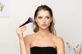 Front view of a thoughtful sensual young woman holding a make-up brush