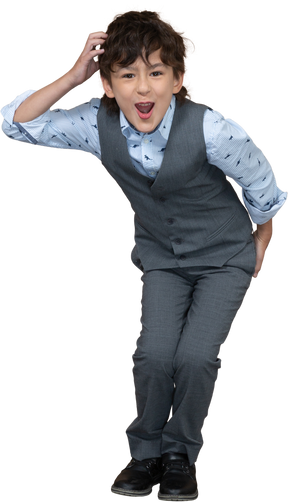 Front view of a happy boy in grey suit squatting and looking at camera