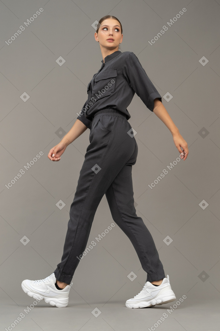 Side view of a walking young woman in a jumpsuit looking aside