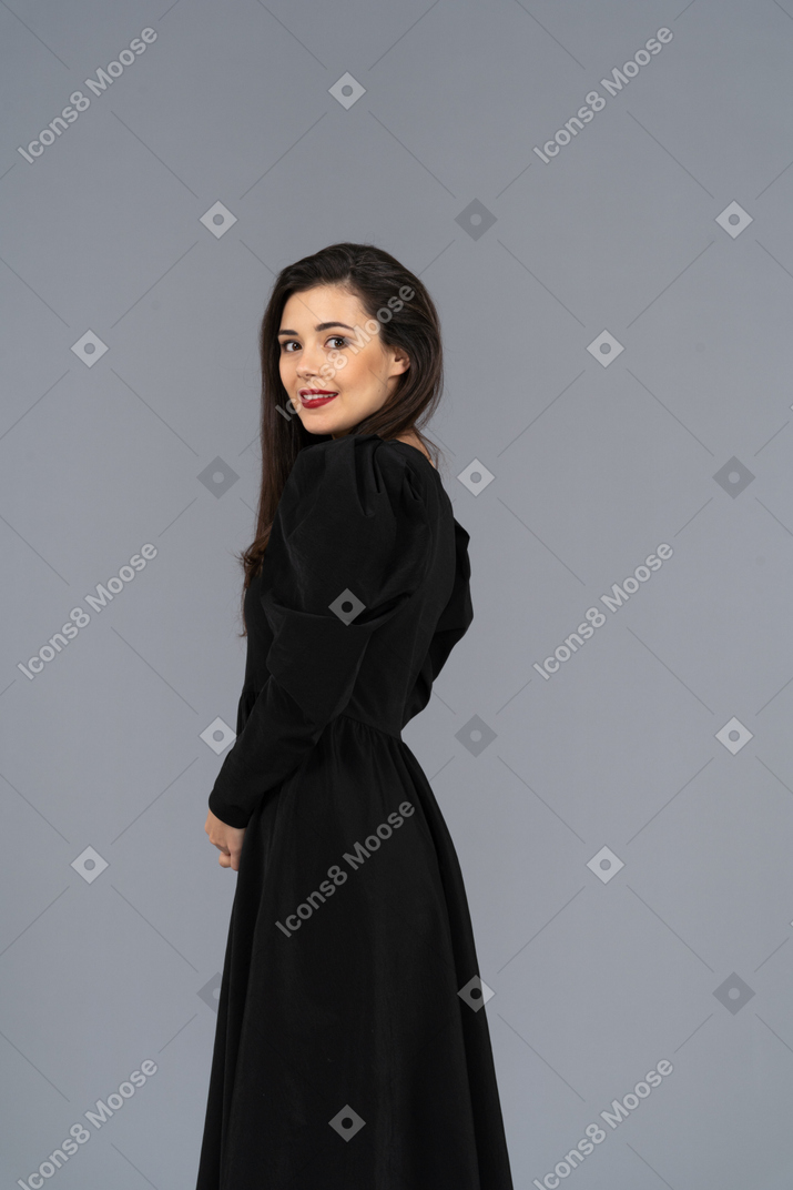 一位年轻的女士，穿着黑裙子站着，看着相机的侧视图