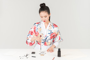 Mujer joven en un colorido kimono japonés aprende caligrafía dibujando un jeroglífico